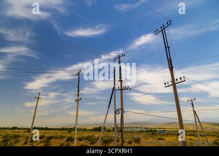 Plusieurs poteaux électriques se dressent haut dans un paysage rural serein. Les lignes électriques s'étendent à travers le terrain plat et sec sous un ciel bleu clair, avec m lointain Banque D'Images