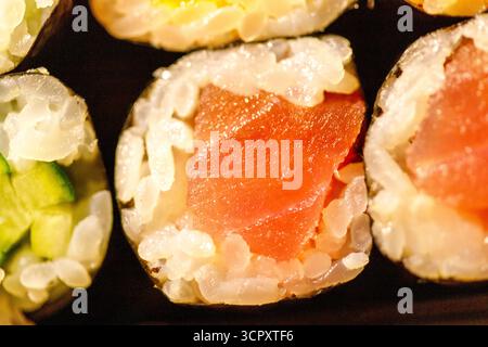 Gros plan macro de rouleaux de sushi assortis, mettant en vedette des garnitures vibrantes de thon et de concombre vert sur riz blanc et nori foncé. Banque D'Images