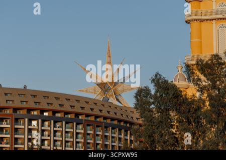 Une grande sculpture d'étoile squelettique domine l'arrière-plan d'une scène urbaine avec des bâtiments modernes et des arbres sous un ciel bleu clair. Banque D'Images