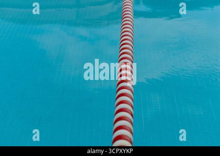 Une ligne de voie de piscine s'étend verticalement à travers l'eau bleue. Les reflets visibles dans l'eau créent un effet ondulé et texturé. Banque D'Images