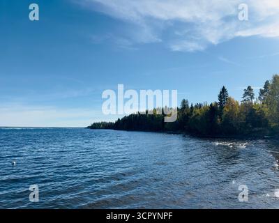 Vue panoramique sur un lac serein avec des arbres verdoyants sous un ciel bleu clair. Banque D'Images