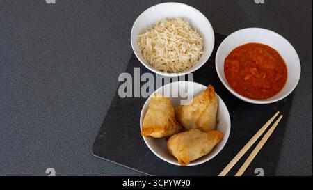 Boulettes dorées frites avec sauce piquante et riz au jasmin servies sur une planche d'ardoise foncée avec des baguettes Banque D'Images