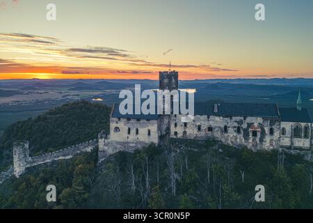 Le château de Bezdez se dresse majestueusement sur une colline, avec ses anciennes tours silhouettées contre un coucher de soleil vibrant. La lumière du soir met en valeur l'architecture médiévale du château et le paysage environnant. Banque D'Images