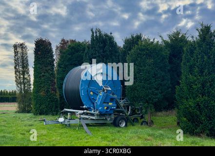 Machine d'irrigation agricole avec grand enrouleur de tuyau sur les terres agricoles vertes et le ciel nuageux Banque D'Images