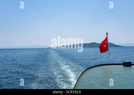Vue panoramique depuis un bateau avec drapeau turc naviguant vers des îles lointaines. Navire se déplaçant à travers la mer bleue calme avec drapeau turc agitant fièrement Banque D'Images