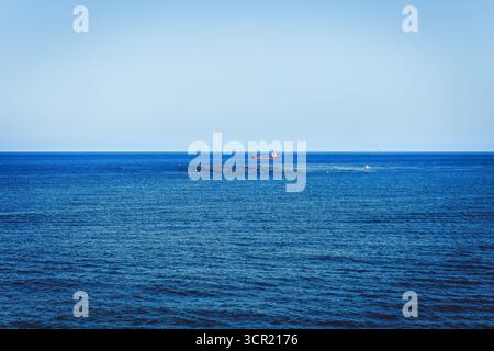 Océan bleu serein sous le ciel avec bateau de pêche rouge lointain, capturant la vie marine tranquille et l'industrie. Plan grand angle de l'immensité Banque D'Images
