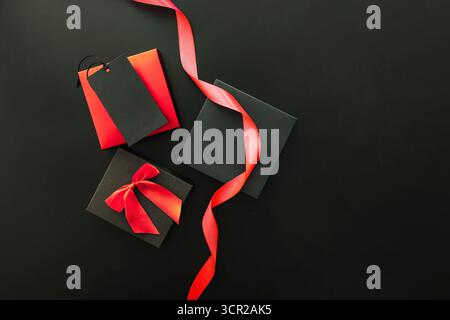 Articles en solde du vendredi fou, y compris des boîtes-cadeaux en noir et rouge, un ruban rouge et une étiquette-cadeau sur fond sombre. Banque D'Images