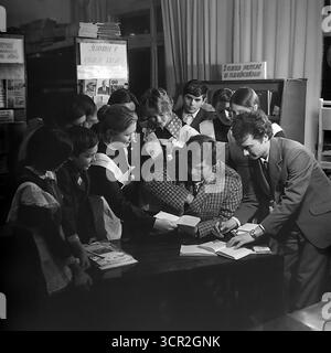 Un groupe d'écoliers enthousiastes en uniforme se réunit autour d'une table avec leurs enseignants et un auteur invité ou invité spécial dans une bibliothèque scolaire à Sloviansk, RSS d'Ukraine, vers 1985. Cette photographie atmosphérique en noir et blanc capture l'excitation d'un événement littéraire, une partie commune de l'éducation soviétique, symbolisant l'importance des livres et de l'apprentissage, et représentant l'esprit curieux et de recherche de connaissances de la jeunesse dans le Donbass pacifique. Banque D'Images
