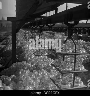 Un système de convoyeur à chaîne aérienne transporte des isolateurs en verre nouvellement fabriqués sur des transporteurs à plusieurs niveaux au-dessus d'une énorme pile de produits finis à l'usine d'armature et d'isolation de Slavyansk (AIZ), vers 1985. Cette magnifique photographie en noir et blanc de Sloviansk, en RSS d'Ukraine, illustre avec force l'immense ampleur de la production de masse soviétique, créant un schéma rythmique d'approvisionnement sans fin et symbolisant le rôle vital de l'usine dans la création de composants pour les vastes réseaux de communication et électriques de la nation dans le Donbass pacifique. Banque D'Images