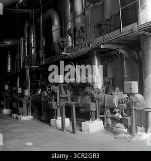 Un réseau complexe de tuyaux industriels de grand diamètre, de vannes massives et de pompes à l'intérieur d'un atelier, peut-être la chaudière, de la Slavyanskaya GRES (centrale régionale d'État) à Mykolaivka, RSS d'Ukraine, vers 1985. Cette photographie atmosphérique en noir et blanc capture l'ingénierie complexe et robuste d'une centrale thermique soviétique, mettant en valeur l'infrastructure vitale qui contrôlait le flux de vapeur et d'eau à haute pression, et symbolisant la puissance industrielle confinée du Donbass pacifique. Banque D'Images