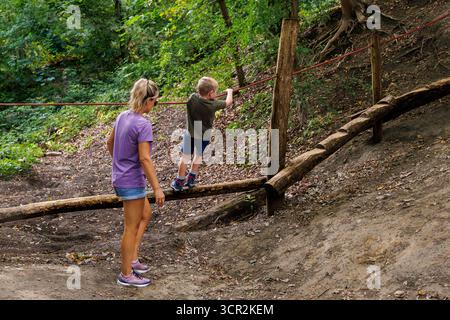 Enfants jouant sur le toboggan et les cordes d'escalade dans une aire de jeux naturelle entourée d'arbres. Banque D'Images