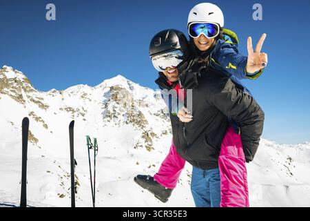 Jeune heureux portrait de couple caucasien ensemble piggyback câlin appréciant de regarder la caméra dans les montagnes enneigées du caucase en hiver. Partez en vacances au ski Banque D'Images