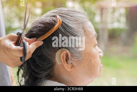 Vue de côté gros plan d'une femme faisant une coupe de cheveux à sa grand-mère à l'extérieur. Mise au point sélective. Banque D'Images