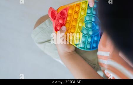 Rainbow push pop it bulle jouet fidget sensoriel dans les mains de l'enfant sur son sol avec espace de copie. Jouets sensoriels en silicone pour autisme, Fidget Popper. Banque D'Images