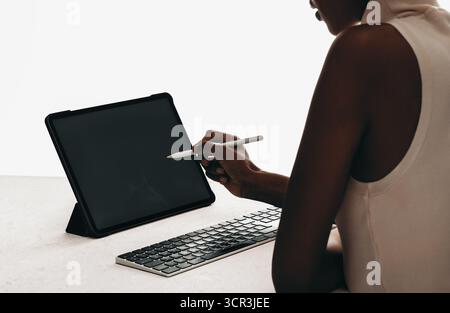 Gros plan d'une femme utilisant un stylet sur une tablette numérique avec clavier dans un espace de travail minimaliste. Idéal pour les maquettes d'appareils, les projets de conception, l'art numérique Banque D'Images