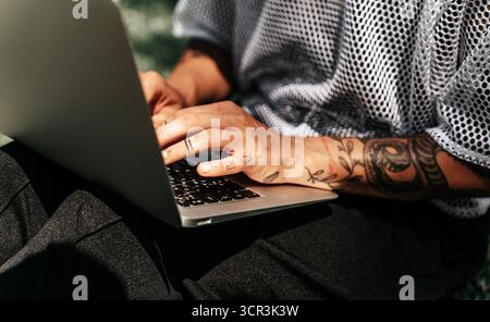 Gros plan de mains féminines tatouées travaillant sur un ordinateur portable à l'extérieur Banque D'Images