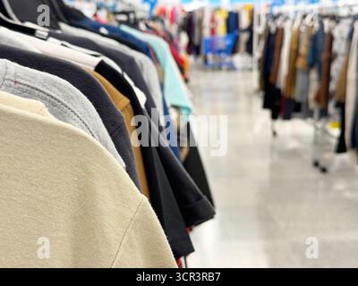 vêtements suspendus sur un rack dans un magasin de vêtements avec plus de vêtements visibles en arrière-plan Banque D'Images