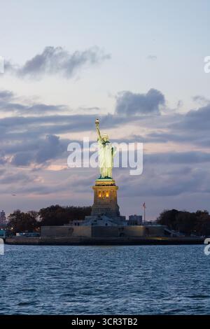 Statue de la liberté au coucher du soleil avec un ciel spectaculaire et une lumière dorée chaude se reflétant sur le monument Banque D'Images