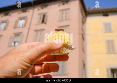 Un homme tient dans sa main un bonbon italien traditionnel appelé Polenta e Osei, avec les façades de couleur pastel de Citta Alta à Bergame apparaissant floues Banque D'Images