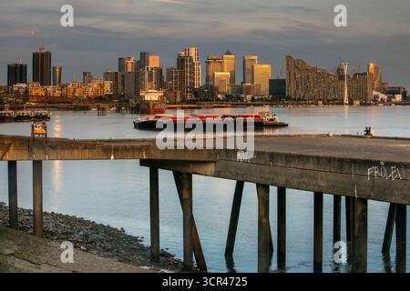 Horizon urbain au coucher du soleil reflété sur une rivière calme avec un pont en béton au premier plan. Canary Wharf, Londres, Royaume-Uni Banque D'Images