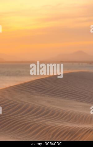 Dunes de sable au coucher du soleil avec un ciel chaud et orange et des montagnes lointaines. KE GA, Binh Thuan, Indonésie Banque D'Images