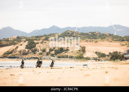 Trois motos garées sur une plage de sable avec des collines lointaines et des éoliennes en vue. Plage près de Phan rang, Ninh Thuan, Vietnam Banque D'Images