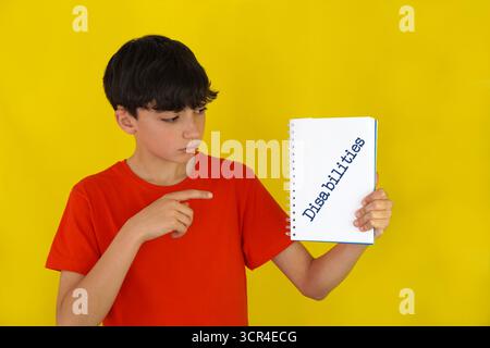 enfance et handicaps. Garçon preteen pointant vers un cahier avec le mot écrit dessus. Banque D'Images