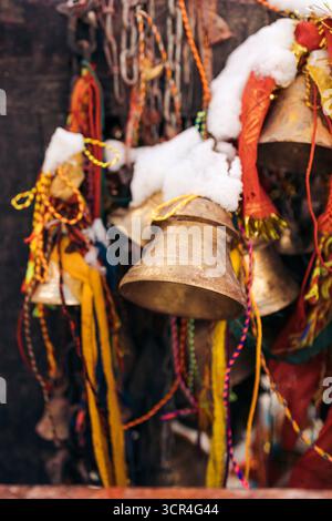 Cloches recouvertes de neige, ornées de rubans colorés et de tissus dans un cadre extérieur. Muktinath, Annapurna, district de Mustang, province de Gandaki, Népal Banque D'Images