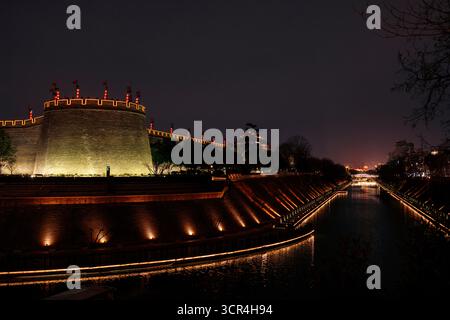 Muraille antique illuminée la nuit avec canal et arbres, un paysage urbain serein en soirée. XI'an, Chine Banque D'Images