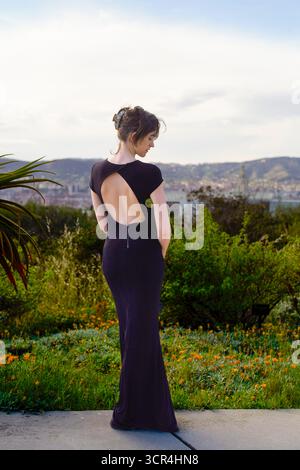Femme dans une robe noire se tient à l'extérieur avec des collines en arrière-plan. Banque D'Images