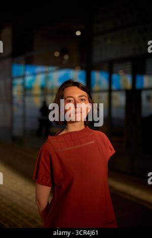 Femme dans une robe rouge se tient sous des lumières chaudes sur une rue pavée. Bruxelles, Belgique Banque D'Images