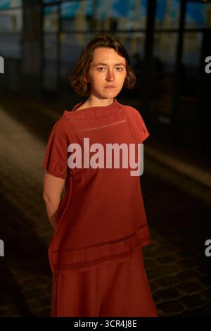 Femme dans une robe rouge se tient sous des lumières chaudes sur une rue pavée. Bruxelles, Belgique Banque D'Images