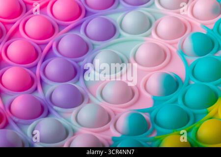 Gros plan d'un jouet fidget en silicone multicolore POP it avec des bulles arc-en-ciel pastel, créant un fond ou une texture éclatant et ludique. Banque D'Images
