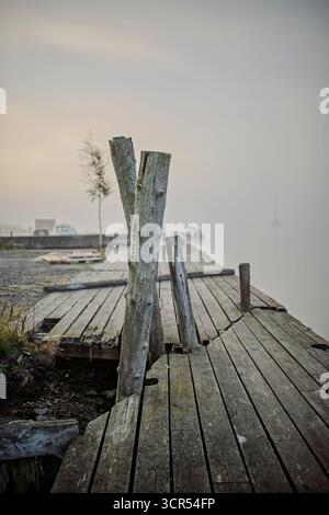 Jetée en bois au bord de la mer, un voilier dans la brume lourde. Banque D'Images