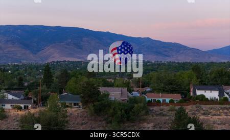 Vue aérienne d'une montgolfière patriotique dérive au-dessus du paysage de banlieue, avec des montagnes en toile de fond, Reno, Nevada, États-Unis. Banque D'Images
