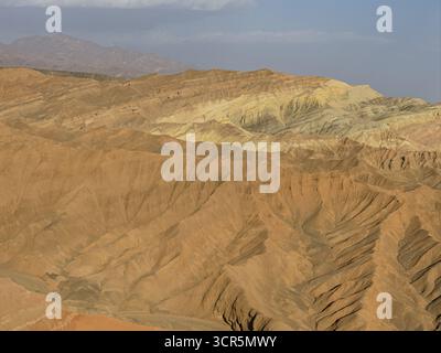 Vue aérienne de la terre dure et ensoleillée de la vallée de Huoyun révèle une tapisserie d'ocre et de beige, sculptée par le temps et les éléments, Turpan, Chine. Banque D'Images
