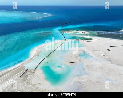 Vue aérienne du contraste frappant entre l'océan sombre et les terres nouvellement récupérées, avec des barrières sombres définissant les bords, Gulhi, Atoll de Malé Sud, Maldives. Banque D'Images