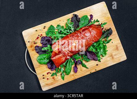 Porc cuit brillant avec mélange de salade, assaisonnements sur planche de bois, sur nappe noire. Vue latérale. Image pour le menu du restaurant. Viande délicieuse. Banque D'Images