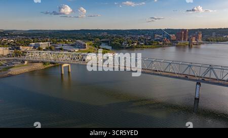 Vue aérienne du pont qui s'étend sur l'eau, avec la ligne d'horizon de la ville en arrière-plan, baignée par la lueur chaude du soleil couchant, Cincinnati, Ohio, États-Unis. Banque D'Images