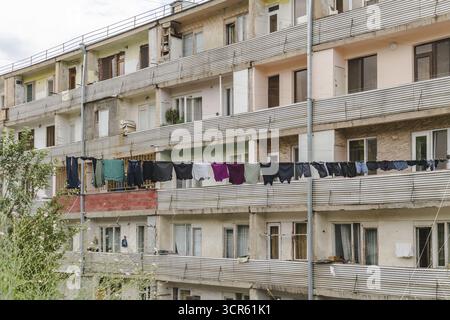 Vue du linge accroché sur les balcons d'un immeuble d'appartements à plusieurs étages altéré, contrastant avec le ciel nuageux, Vayk, province de Vayots Dzor, Arménie. Banque D'Images