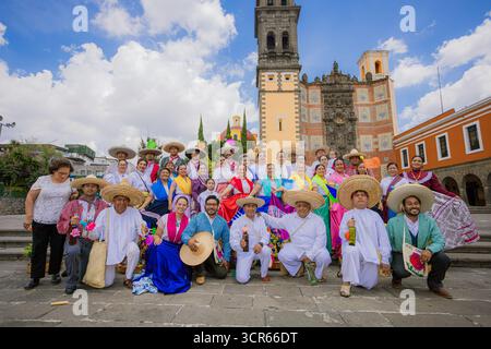 Grand groupe de danseurs et de personnes portant des costumes mexicains traditionnels posant devant une église historique sous un ciel bleu avec des nuages. Banque D'Images