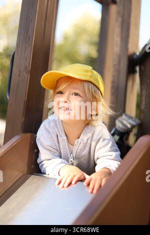 Mignon garçon de trois ans souriant tout en étant allongé sur un toboggan pour enfants. Banque D'Images