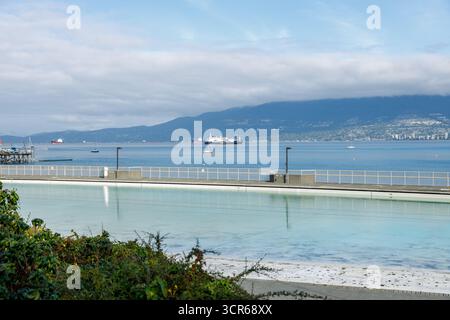 Vancouver, Canada - 15 septembre 2025 : vue panoramique de la piscine Kitsilano avec des nageurs profitant de l'eau, encadrée par un front de mer serein, des montagnes lointaines, et Banque D'Images