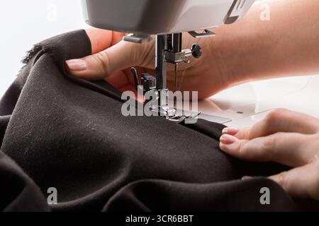 Couturière travaillant sur un tissu noir à l'aide d'une machine à coudre dans un espace de travail lumineux et confortable Banque D'Images