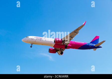 Vue en bas angle d'un Airbus A321 rose et bleu de Wizz Air en vol contre un ciel bleu. Banque D'Images