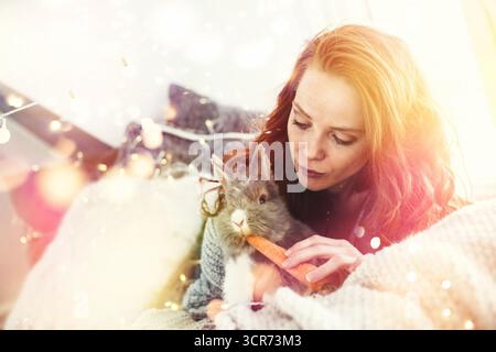 Lapin domestique (Oryctolagus cuniculus F. domestica), femme câlin avec un lapin et lui donnant une carotte Banque D'Images