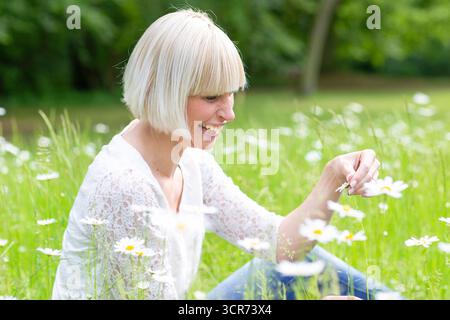 Femme heureuse assise sur un pré tenant une Marguerite à la main Banque D'Images