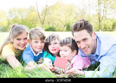 Famille avec trois enfants sur une prairie planifiant une maison individuelle Banque D'Images
