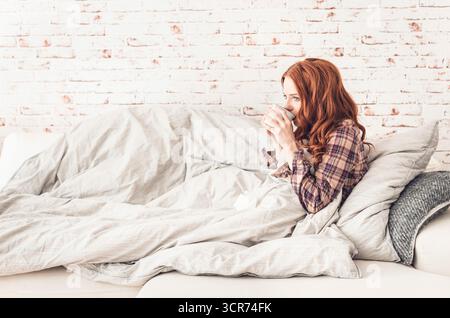 femme malade assise sur le canapé buvant une tasse de thé Banque D'Images