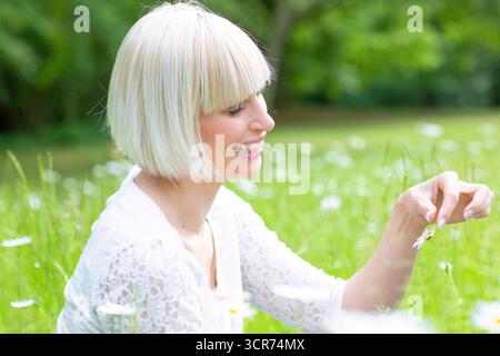 Femme heureuse assise sur un pré tenant une Marguerite à la main Banque D'Images